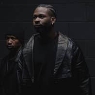 Very darkly lit photo of 2 men in dark clothing so barely visible.