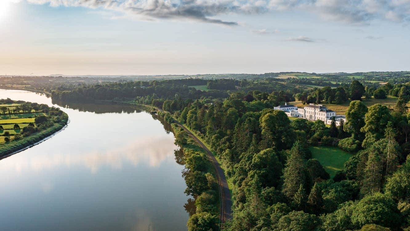 Aerial view of large estate house surrounded by trees and a lake in front
