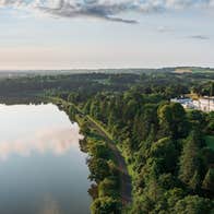 Aerial view of large estate house surrounded by trees and a lake in front