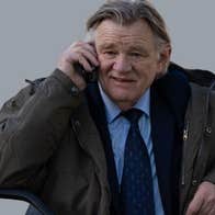 An older man in suit and tie with bulky overcoat is talking on a mobile