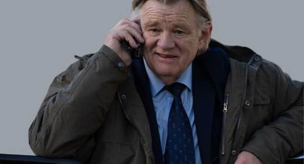 An older man in suit and tie with bulky overcoat is talking on a mobile