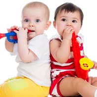 2 babies seated back to back with plastic wind instruments