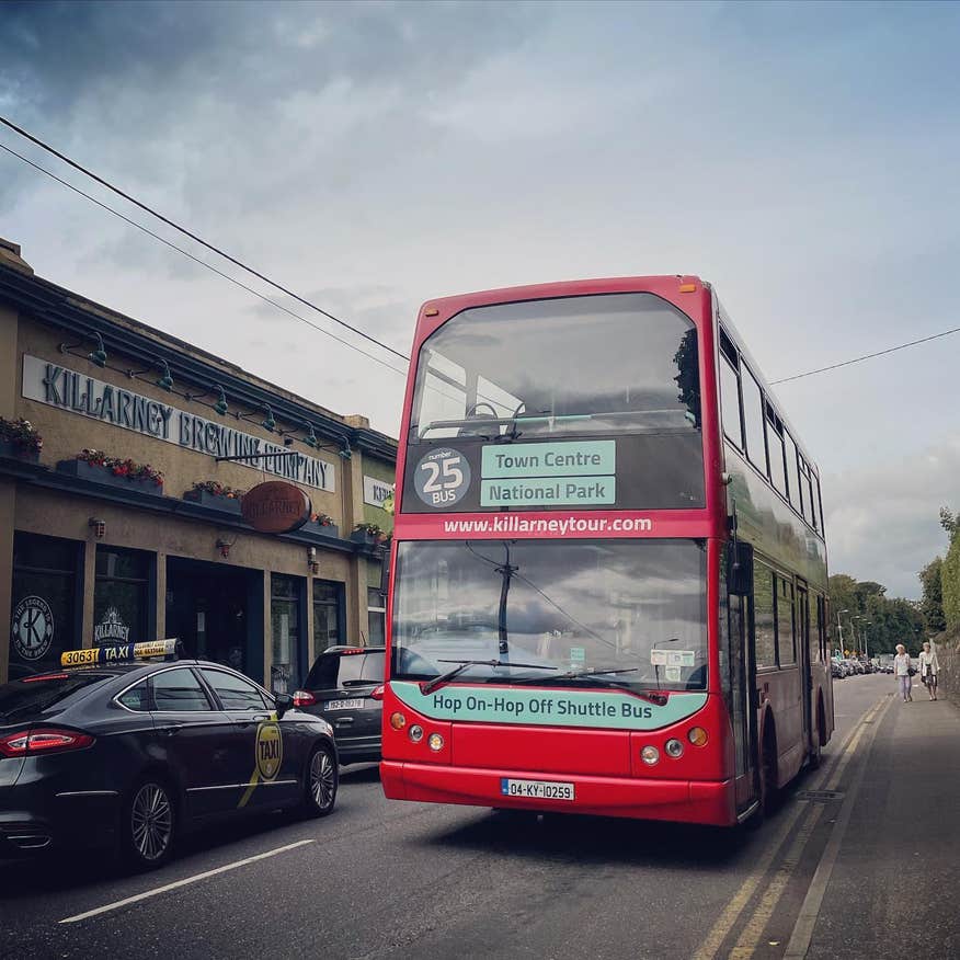 A Big Red Bus from Killarney Tours in County Kerry driving down a street.