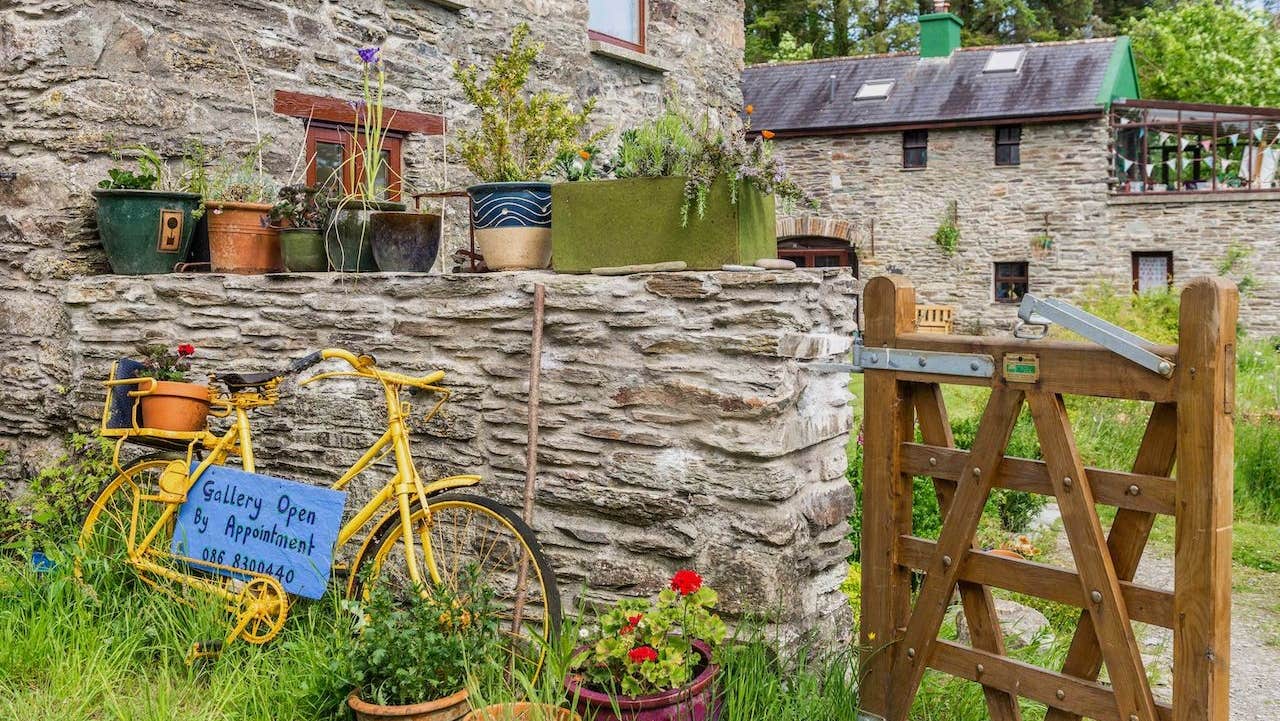 A stone wall with colourful plants and a large stone farm building in the background