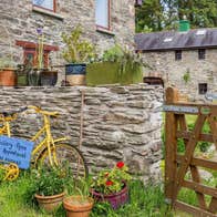 A stone wall with colourful plants and a large stone farm building in the background