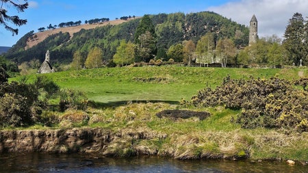 Round tower and ruins of a church in a field next to a stream