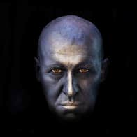 UNDERNEATH written and performed by Pat Kinevane - a bald man's face in silver colour surrounded by blackness.