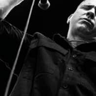 Black and white image looking up at a serious looking man, holding a mic.