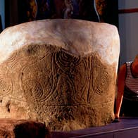 A woman looking closely at an artistic engraving on a stone.
