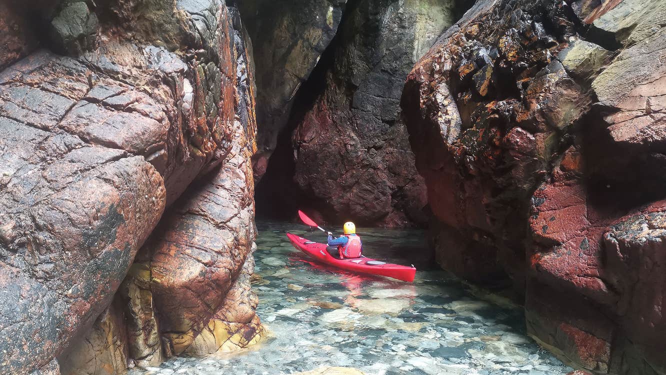 Sea Kayaking Donegal kayaker on the water near a colourful rocky inlet