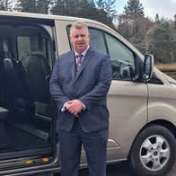 A chauffeur in a suit posed at his mini van