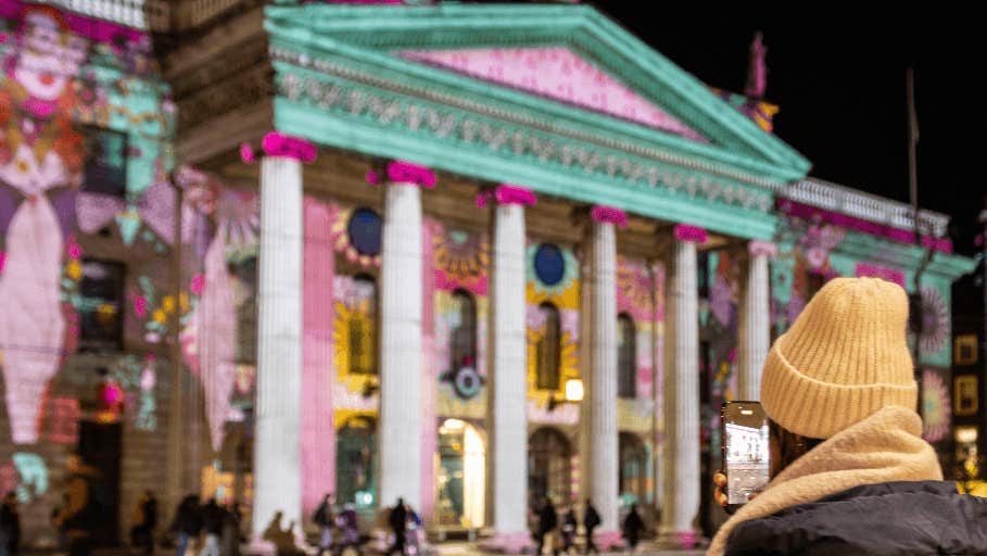 Brigit 2026: Illuminating the GPO - view of a large building with tall columns at night covered in light show with rear view of person looking on.