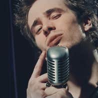A man singing into large old style mic with eyes shut.