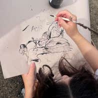 Looking down at young child holding a pen creating a black pen and ink picture.