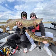 Two anglers holding large pike aboard a fishing boat on a lake
