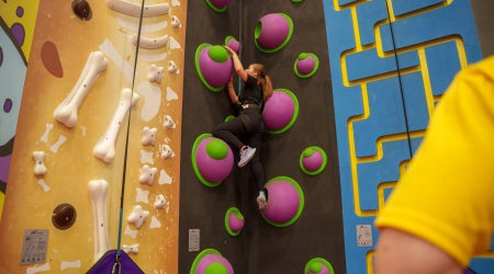 A wall with climbing frames in various shapes and colours with someone climbing