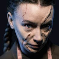 A woman with scarred SFX makeup looks sinisterly into the camera