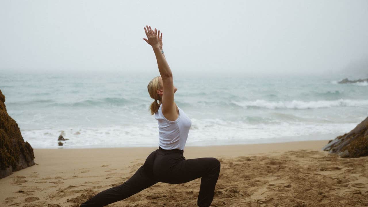 Lady doing a yoga stretch on the beach with the sea in the background