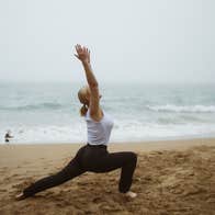 Lady doing a yoga stretch on the beach with the sea in the background