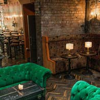 Green velvet seating area in an inviting lounge with candlelit tables and exposed brick walls