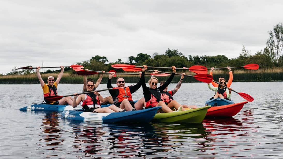 Group of people holding paddles over their heads while kayaking on the River Shannon in Leitrim.