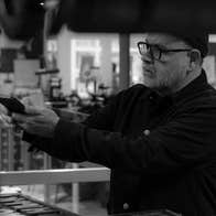Anthony Burrill and Maser In Conversation, a man in a museum holding his mobile phone horizontally out in front of him with various print machines in the background.