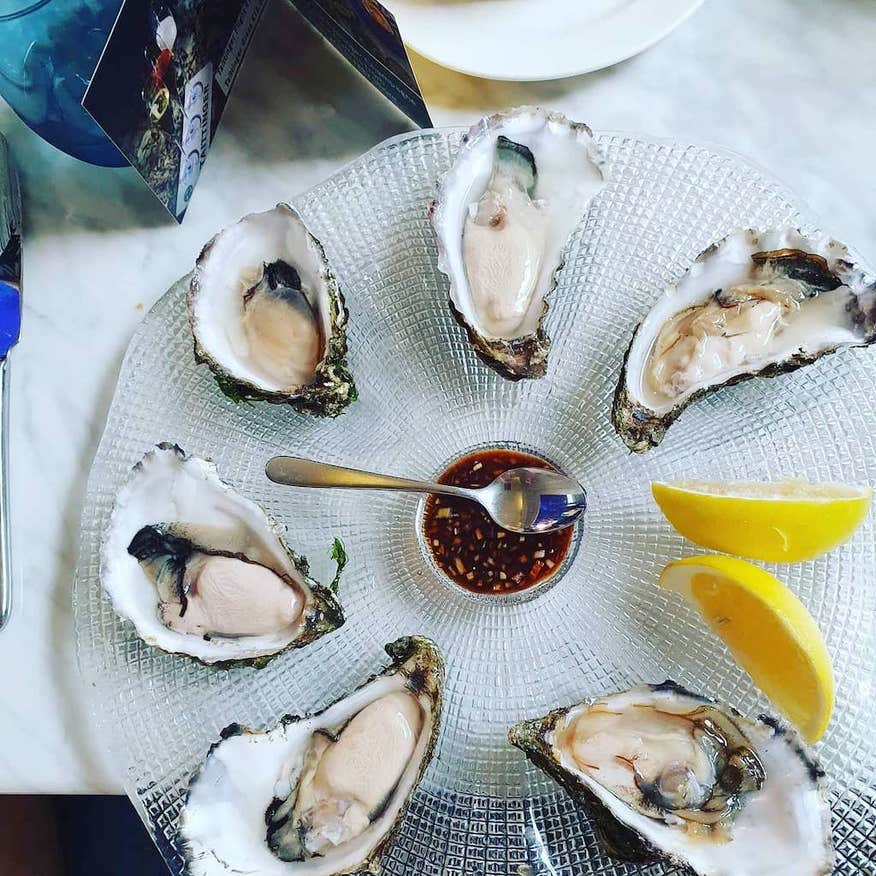 Oysters displayed on a clear glass platers garnished with lemon wedges and a chilli dressing in the middle.