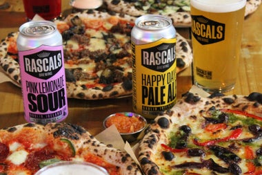 Colourful pizza on dishes ready to eat along with some branded cans of drink