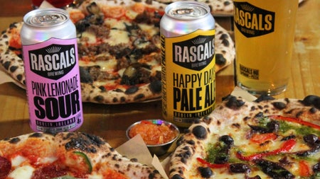 Colourful pizza on dishes ready to eat along with some branded cans of drink