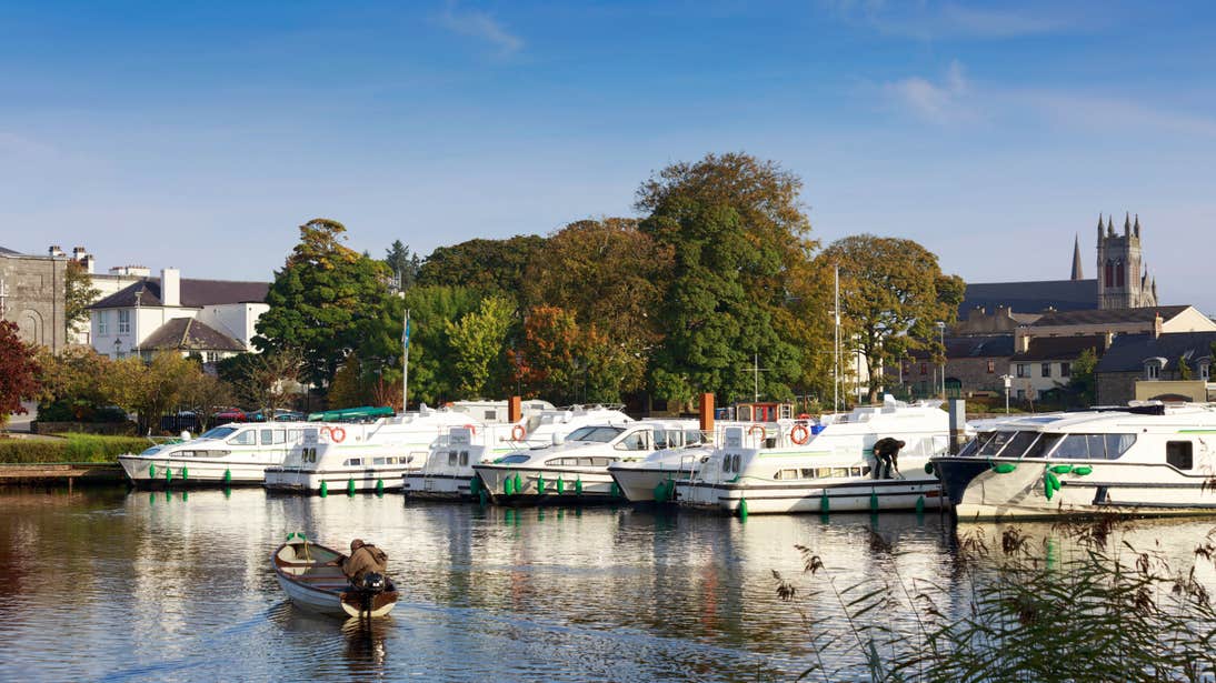 Boats in a marina with a backdrop of trees and a church in Carrick-on-Shannon, Leitrim