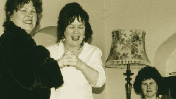 Old photo of 2 women standing and laughing with seated woman holding pipes.