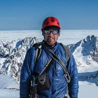 A man in mountaineering gear including helmet and sunglasses on snowy mountain
