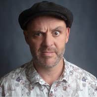 A confused looking man wearing a flat cap and patterned shirt.