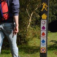 A person with a backpack walking on a path with a trail marker sign