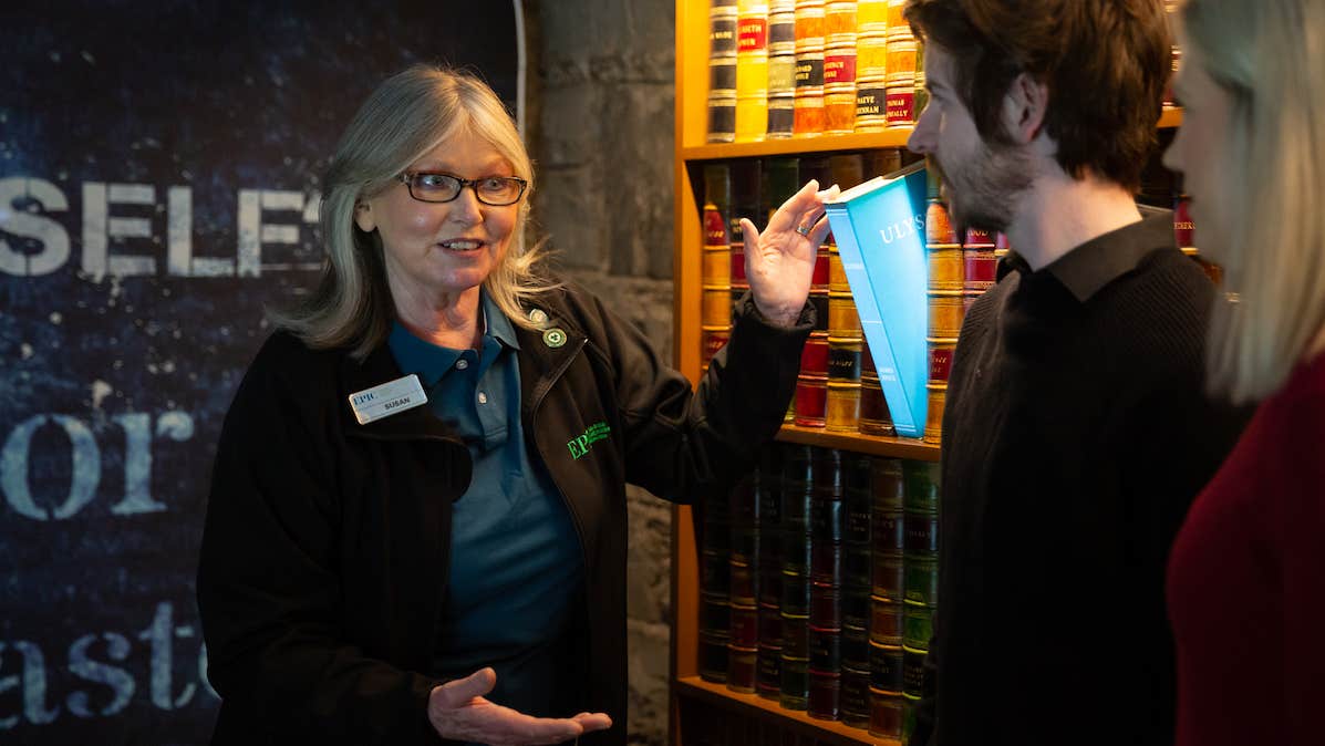 A tour guide is talking to 2 people standing beside an exhibit.