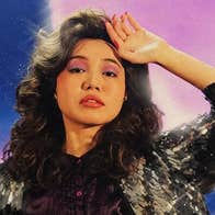 A woman is holding up the back of her hand to her forehead in a slightly dramatic manner.