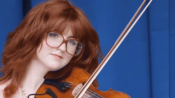 A serious looking young woman holding a violin and bow ready to play