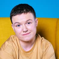 Comedian Sinead Walsh, gently smiling, seated in a yellow, highback armchair.