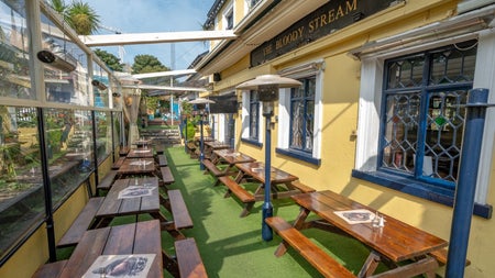 Two rows of wooden picnic benches along the exterior wall of a pub