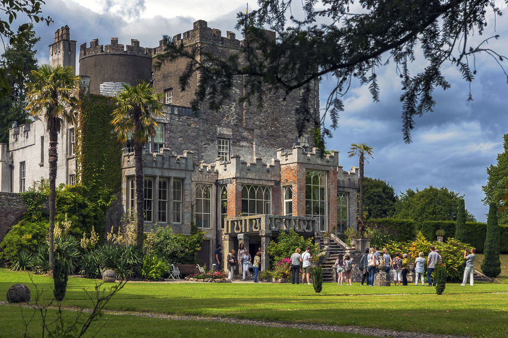 People standing on a lawn outside a castle style country house on a sunny day
