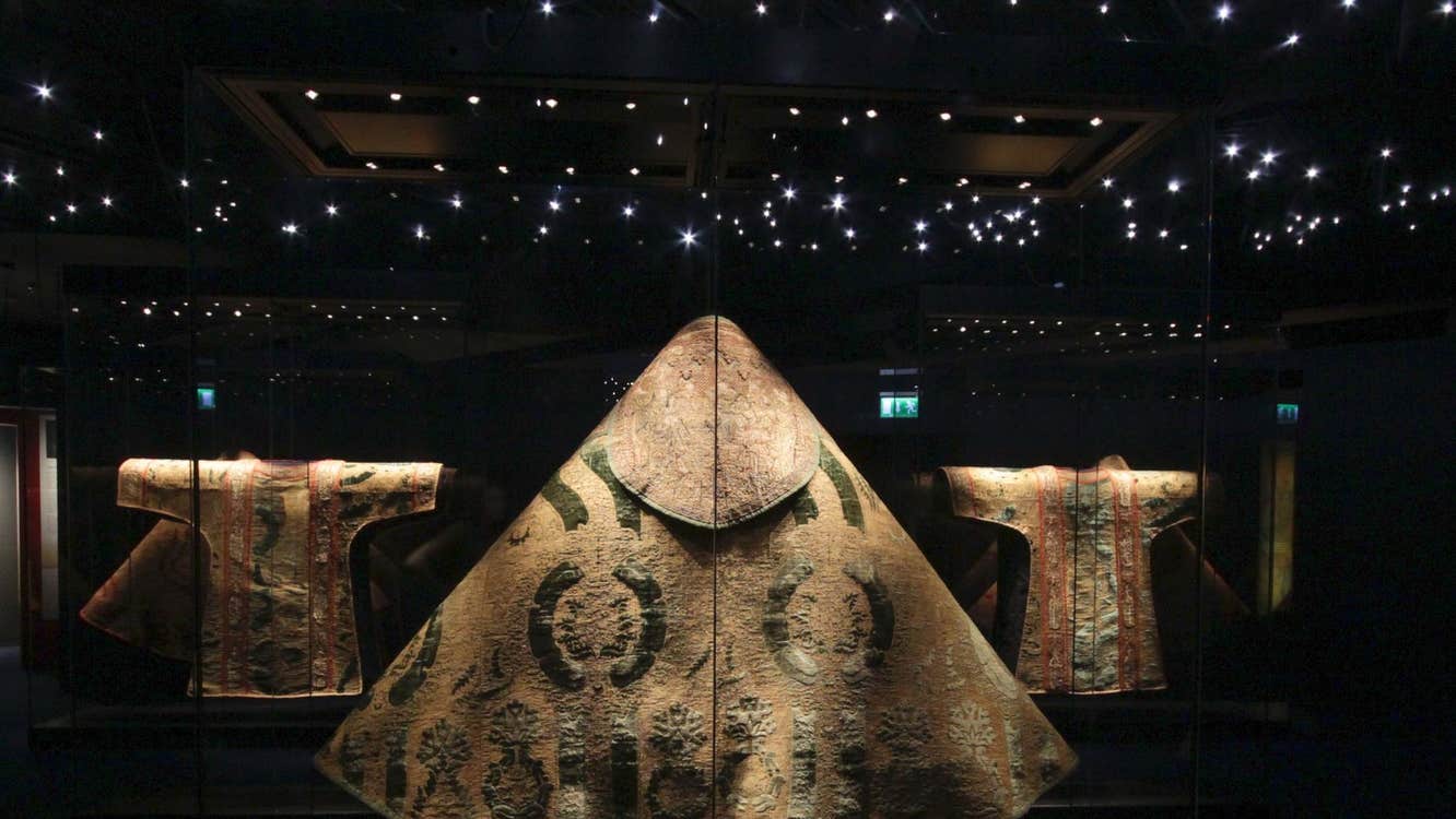 Large gold vestment on display in a dark room with lots of small twinkling lights above it