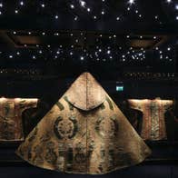 Large gold vestment on display in a dark room with lots of small twinkling lights above it