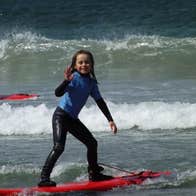 A young girl standing on a red surf board in the sea