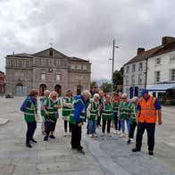 Group wearing green jackets led by a guide in an orange jacket all looking at the ground in Athy