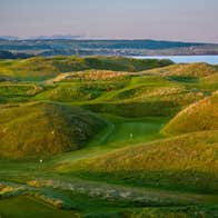 A golf course with grassy dunes and the coast in the distance