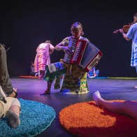 Musicians moving around a stage whilst playing to a seated adult and baby