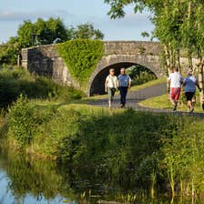 Two couples walk past each other on the Royal Canal Greenway near a stone bridge