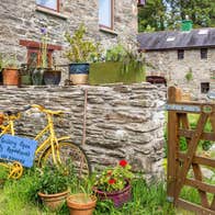 Stone house and wall with a yellow bike resting against it a wooden gate and pots of flowers