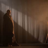 Fishamble presents Silent by Pat Kinevane - a man wrapped in a blanket is looking at old style camera on a tripod