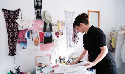 Artist working with materials on a desk with fabrics hanging on the wall